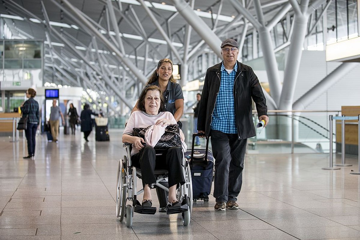 Passagierin mit eingeschränkter Mobilität im Rollstuhl wird von einer Mitarbeiterin im Terminal betreut