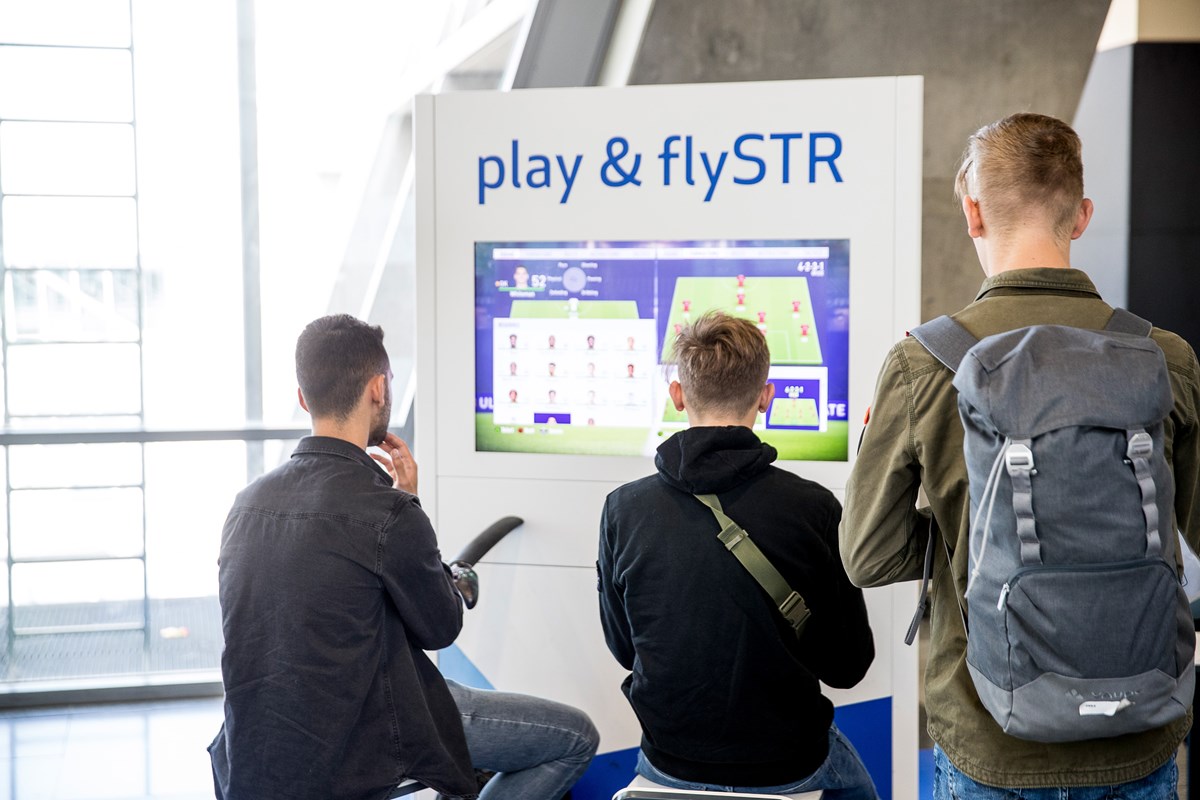 Passagiere spielen an den Spielekonsolen der Gamezone im Terminal