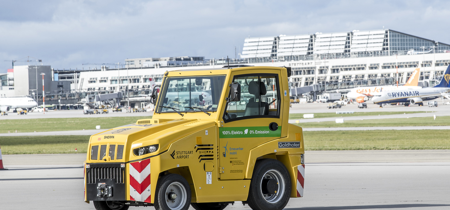 Ein elektrisch betriebener Cargo-Schlepper steht auf dem südlichen Stuttgarter Flughafenvorfeld. Im Hintergrund stehen die Terminalgebäude. 