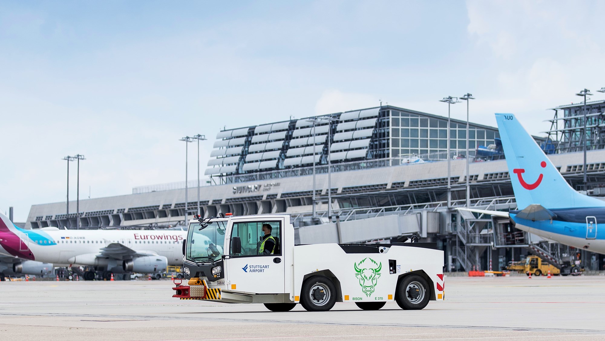 Ein elektrisch betriebenes Pushback-Fahrzeug steht auf dem Stuttgarter Flughafenvorfeld. Im Hintergrund parken Flugzeuge. 