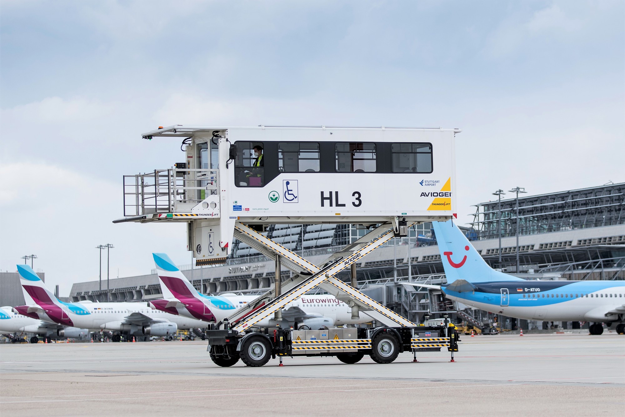 Ein elektrisch betriebener Medical-Highloader steht ausgefahren auf dem Stuttgarter Flughafenvorfeld. Im Hintergrund parken Flugzeuge. 