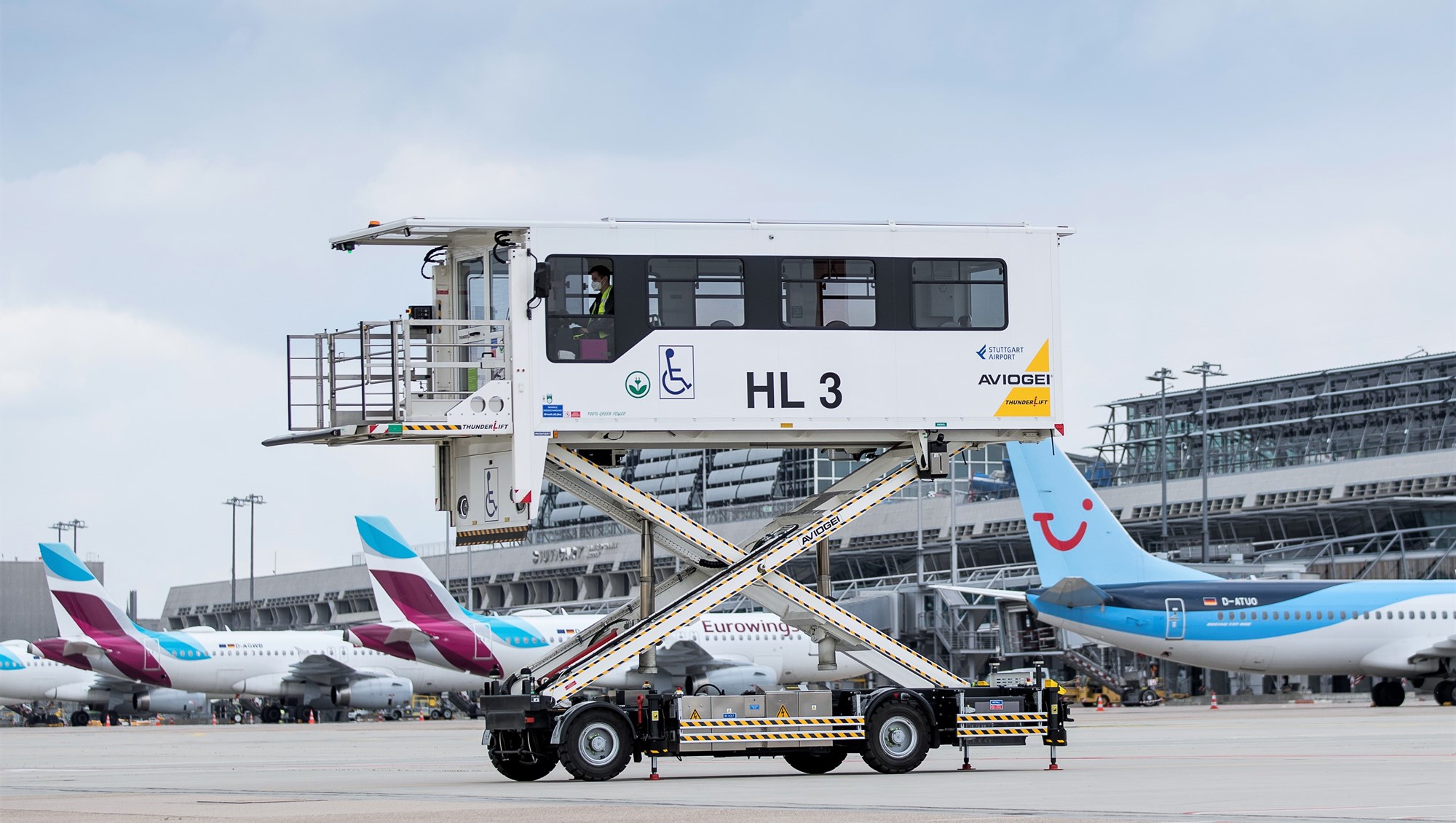 Ein elektrisch betriebener Medical-Highloader steht ausgefahren auf dem Stuttgarter Flughafenvorfeld. Im Hintergrund parken Flugzeuge. 