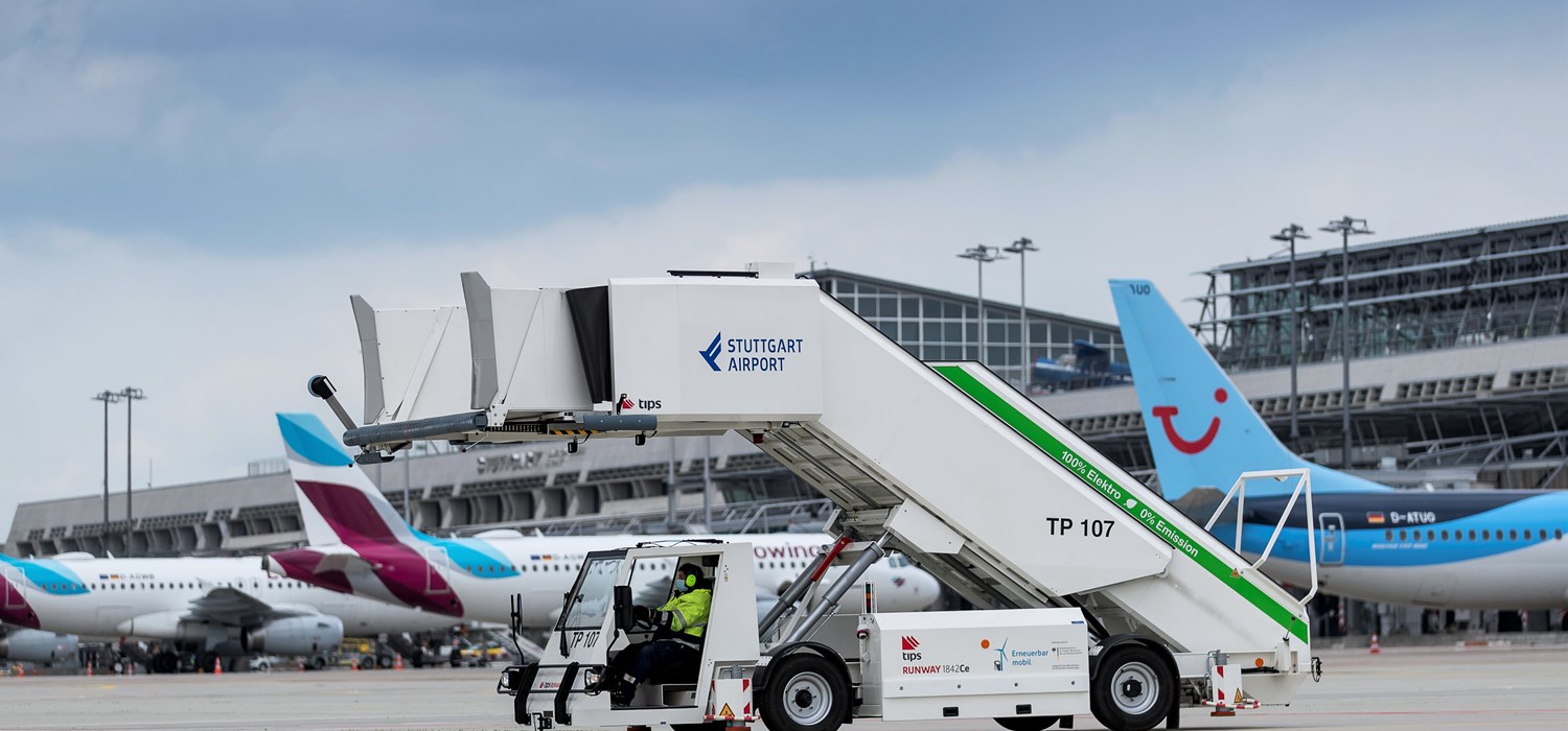 Eine elektrisch betriebene Passagiertreppe steht auf dem Stuttgarter Flughafenvorfeld. Im Hintergrund parken mehrere Flugzeuge. 