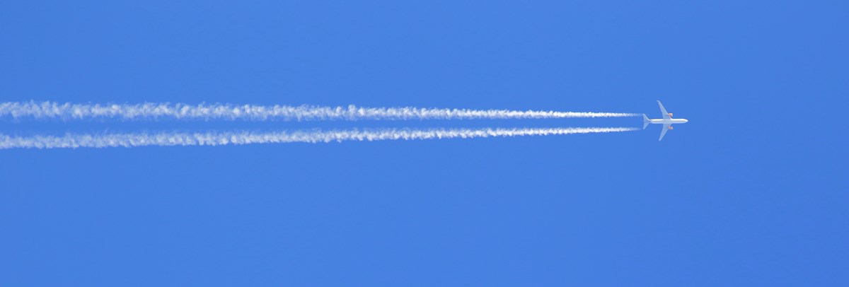 Ein Flugzeug hinterlässt einen weißen Kondensstreifen auf blauem Himmel.