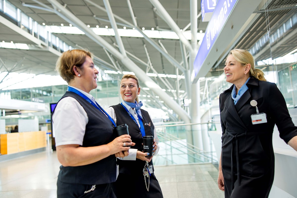 Drei Mitarbeiterinnen des Flughafen Stuttgart stehen am Informationsschalter und sprechen miteinander. 